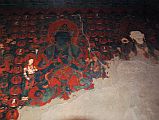 Lo Manthang Thubchen 06-3 Main Assembly Hall Painting Of Blue Buddha To Right Of Door The paintings in the assembly hall at Thubchen Gompa in Lo Manthang consist of twelve triad sets, each with a large, central figure flanked by two smaller standing figures. The second triad to the right of the entrance door of the assembly hall at Thubchen Gompa in Lo Manthang features a blue Buddha in a mudra of teaching. To the right is another white figure.